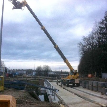 Eine Baustelle mit einem gelben Kran, der seinen Arm in den bewölkten Himmel streckt, umgeben von Material und Maschinen